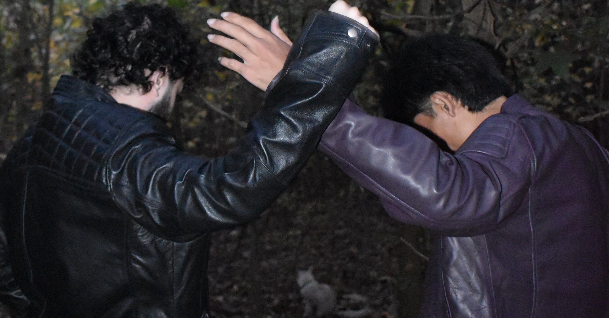 Two people in dark jackets on a forest floor with trees in the background